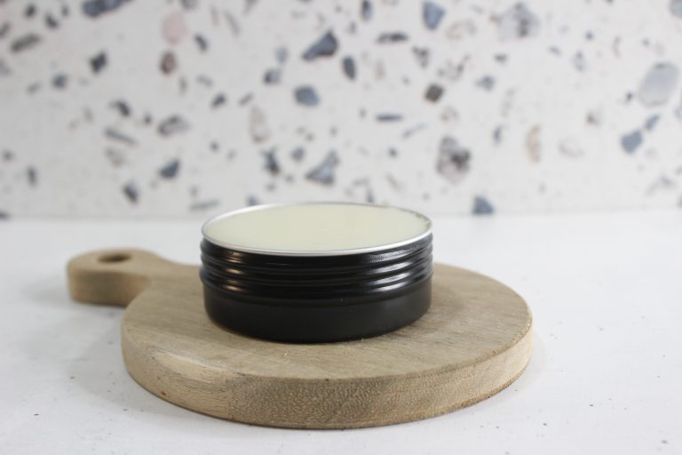 Homemade dog paw balm poured into a black tin, resting on a wooden board with a terrazzo background.